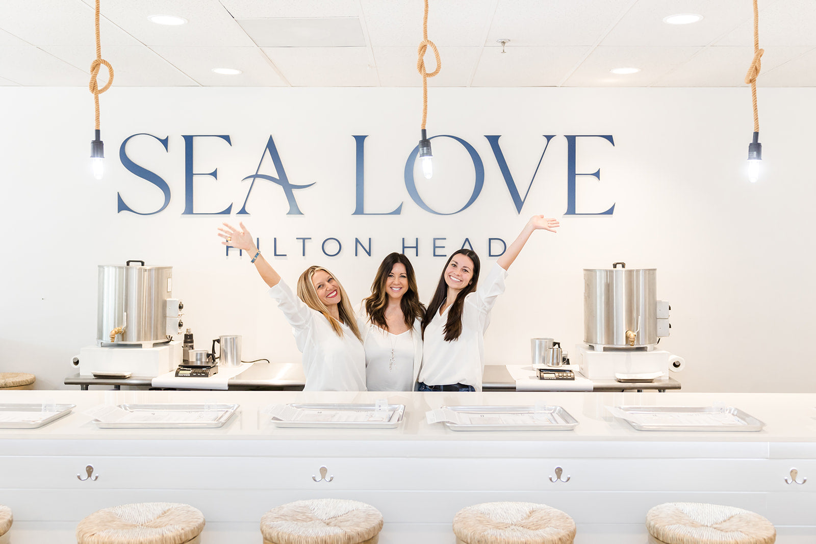 Three joyful women celebrating franchise opportunities at a bright and modern candle bar named "sea love" in hilton head