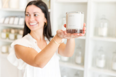 Woman smiling while presenting a scented candle in a boutique-like setting.