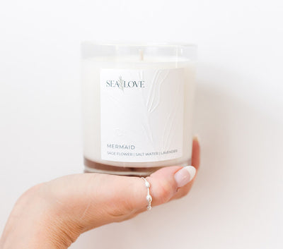 A hand gently holds a scented candle labeled 